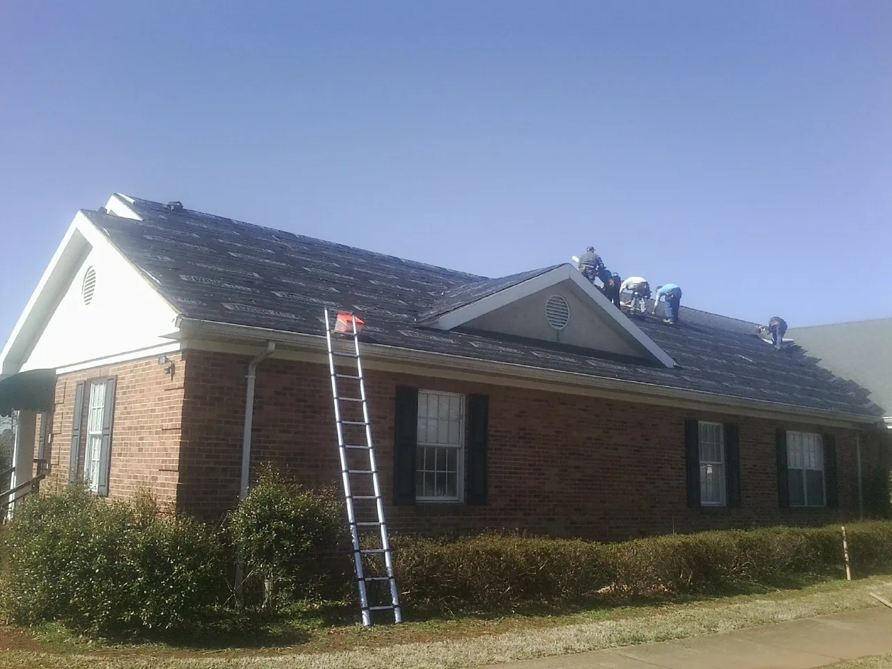 Crew tearing shingles off a brick ranch roof with a ladder set — Emergency Roof Repair work by our crew in Gate