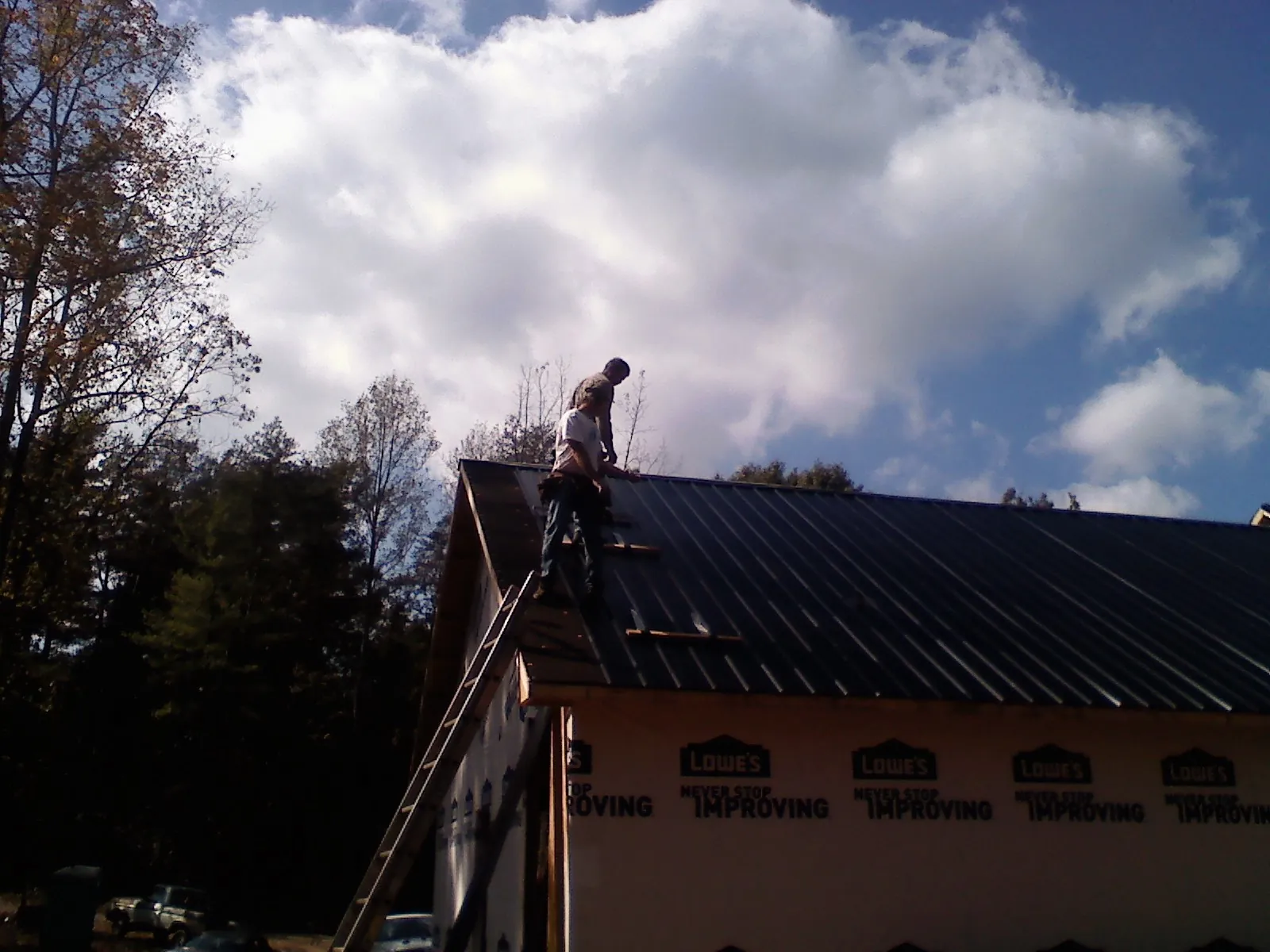 Roofer fastening dark metal panels high against a cloudy sky, from a Roof Inspection job in Gate