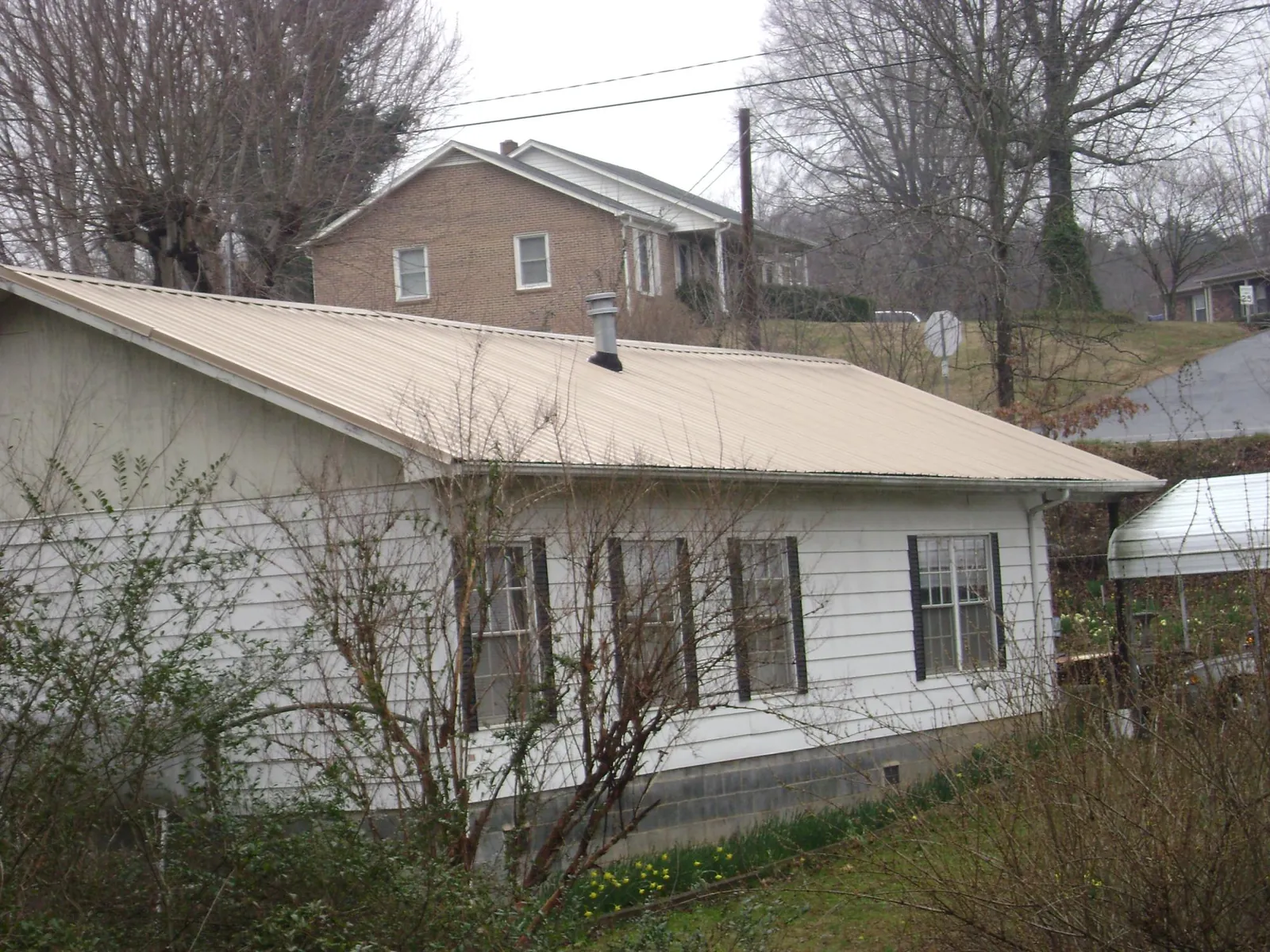 Tan metal roof on a white sided house set into a hillside — Commercial Roofing by Roofing Brothers in Gate
