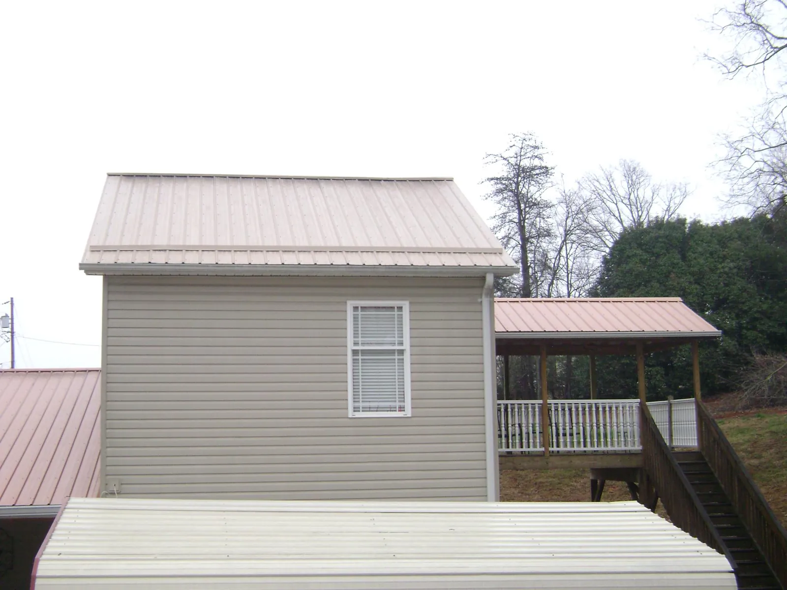 Tan metal roofs on a two story addition and attached porch, from a Roof Replacement job in Gate